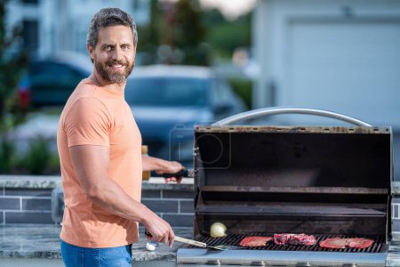 Photo for Man grilling delicious barbecue on a summer day. happy man preparing grilled food at backyard barbecue. ribeye steak. man with hot grill at a barbecue party. Skilled grilling master. - Royalty Free Image