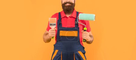 Photo for Cropped man decorator in work clothes hold paint roller and brush on yellow background. - Royalty Free Image