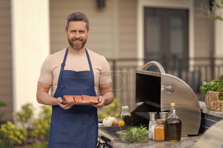 Photo for Man cook salmon on grill, copy space. chef man cooking salmon on grill outdoor. grill salmon fish at man wear apron. photo of man with grill salmon. - Royalty Free Image