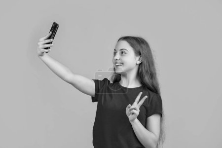 Téléchargez les photos : Heureux enfant faire selfie sur smartphone sur fond jaune. - en image libre de droit