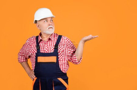 Photo for Serious old man builder in helmet on yellow background. - Royalty Free Image