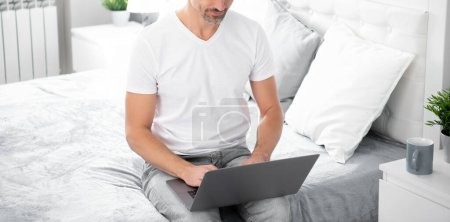 Téléchargez les photos : Mature homme utilisant ordinateur sur lit avec café. - en image libre de droit