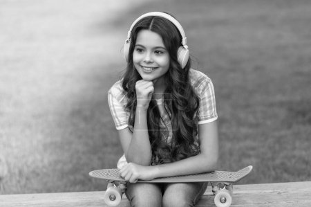 Photo for Smiling teen girl with skateboard outside. photo of teen girl with skateboard listen music. teen girl with skateboard outdoor. teen girl with skateboard in headphones. - Royalty Free Image