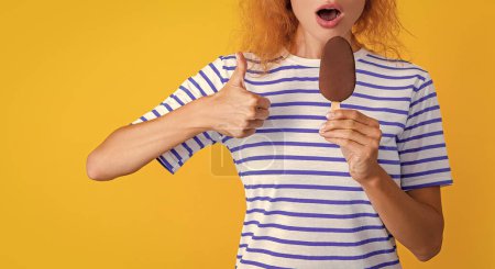 Foto de Vista recortada de chica con delicioso helado, pulgar hacia arriba. foto de chica con delicioso helado en verano. chica con delicioso helado aislado en amarillo. chica con delicioso helado en el estudio. - Imagen libre de derechos