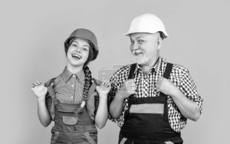 Photo for Cheerful teen child and grandfather builder in helmet on yellow background. - Royalty Free Image