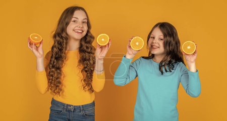 cheerful teen children hold orange fruit on yellow background.