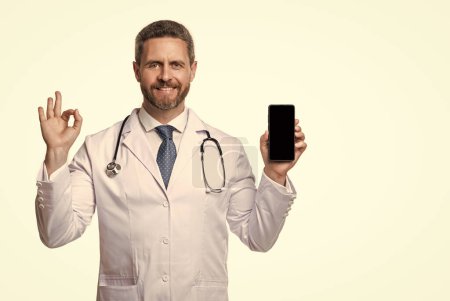 Photo for Medical man show telehealth on background, ok. photo of medical man show telehealth on phone screen. medical man show telehealth isolated on white. medical man show telehealth in studio. - Royalty Free Image