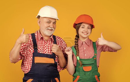 Photo for Happy child and grandfather builder in hard hat on yellow background. thumb up. - Royalty Free Image