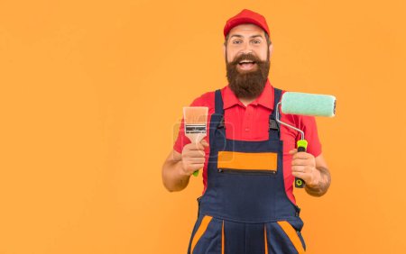 Photo for Amazed bearded man housepainter in work clothes hold paint roller and brush on yellow background. - Royalty Free Image