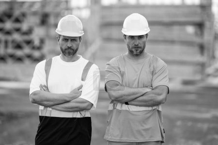 Téléchargez les photos : Travailleurs de la construction sur le chantier. Des hommes sérieux portant des gilets de sécurité et des casques de construction. Contremaître et constructeur. Génie civil croisant les armes. - en image libre de droit