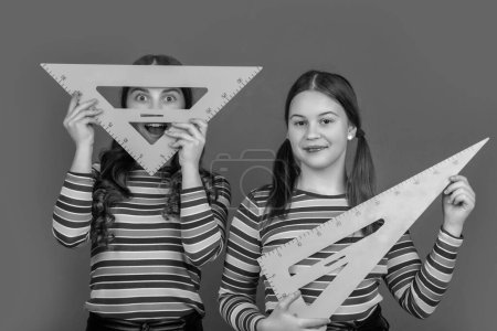 Foto de Niñas sonrientes de la escuela sostienen herramienta matemática de triángulo. - Imagen libre de derechos