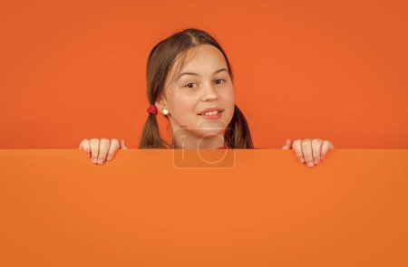 niño sonriente detrás de papel naranja en blanco con espacio de copia para publicidad.