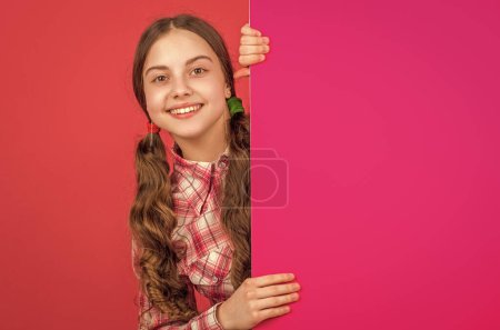 lächelndes Teenie-Mädchen hinter leerem rosa Papier mit Kopierplatz für Werbung.
