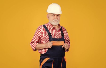 Photo for Serious senior man builder in helmet on yellow background. - Royalty Free Image