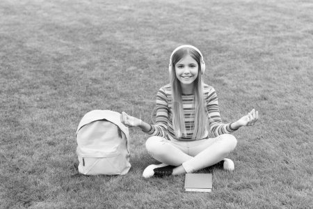 Téléchargez les photos : Meditating teen girl listening to music sitting on grass after school, education. - en image libre de droit