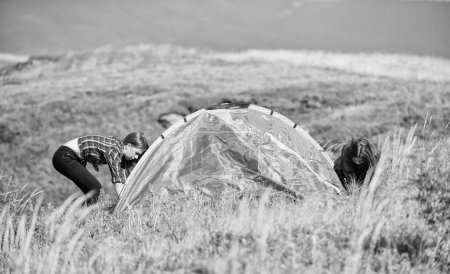 Foto de Girls set up tent on top mountain. Camping trip. Helpful to have partner for raising tent. Camping skills concept. Camping and hiking. In middle of nowhere. Temporary housing. Vacation in mountains. - Imagen libre de derechos