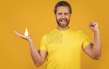 Téléchargez les photos : Homme heureux avec médecine nasale en studio. photo de l'homme avec des gouttes de médecine nasale. homme avec médicament nasal isolé sur jaune. homme avec médecine nasale sur fond. - en image libre de droit
