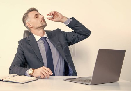 Ältere Mann in Geschäft Büro verwenden Nasentropfen.