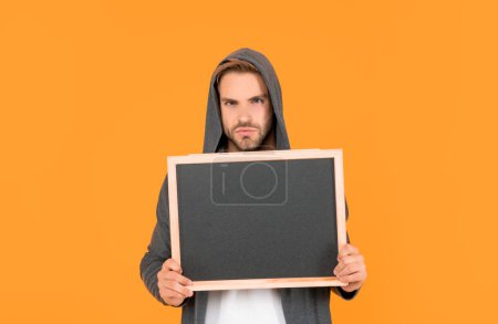 unshaven young man in hood hold blackboard with copy space on yellow background, advert.