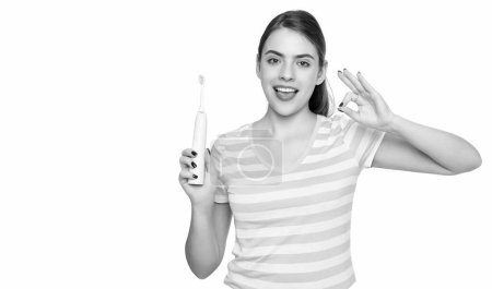 Téléchargez les photos : Happy young woman with electric toothbrush isolated on white background. ok. - en image libre de droit