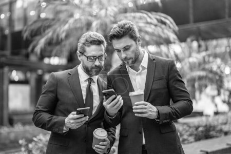 Photo for Business colleagues with stock reports on phone in suit. photo of business colleagues with phone and coffee. business colleagues with phone in the street. business colleagues with phone outdoor. - Royalty Free Image