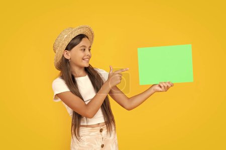happy teen girl with copy space on green paper on yellow background. point finger.