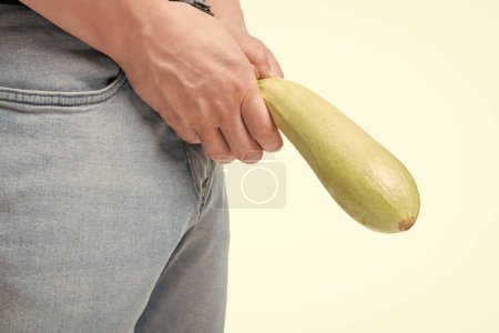 Man crop view holding zucchini as penis at crotch level imitating erectile dysfunction isolated on white.