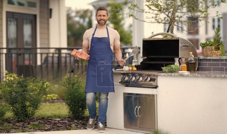 full length of barbecue man with salmon in apron. photo of barbecue man with salmon fish. barbecue man with salmon. barbecue man with salmon outdoor.