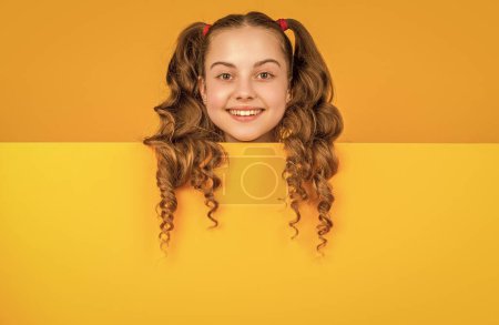 smiling child behind blank yellow paper with copy space for advertisement.
