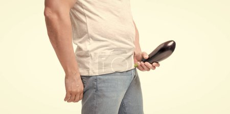 Guy crop view holding eggplant at crotch level imitating erect penis isolated on white.