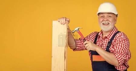 happy mature man woodworker in helmet on yellow background.