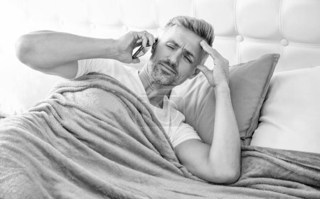 confused mature man in bed speaking on phone.