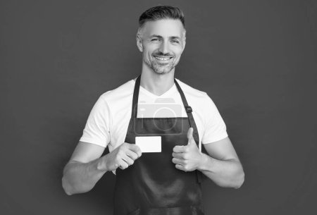 happy mature man in apron with copy space on card. thumb up.