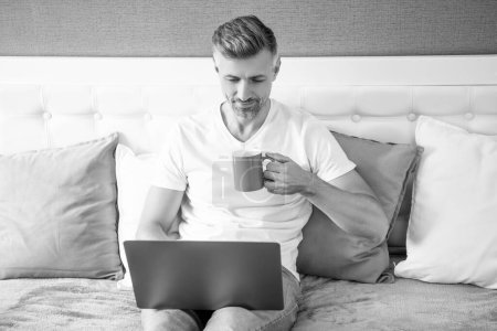 busy mature man using computer in bed with coffee.