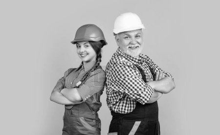 positive child and grandfather builder in helmet on yellow background.
