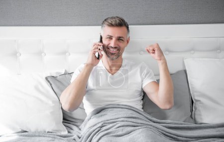 successful mature man in bed speaking on phone.