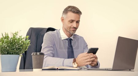 Photo for Mature businessman working in office with smartphone and pc. - Royalty Free Image