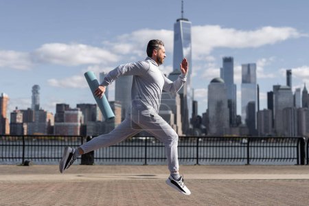 Man in sports suit training jogging running in Manhattan with fitness mat for workout outdoor.