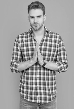 man with pray hand gesture. studio shot of man. caucasian man having stubble. handsome man in checkered shirt isolated on grey background.
