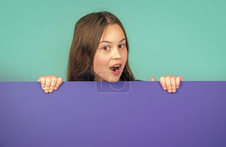 Überraschtes Kind hinter blauem Papier mit Kopierplatz für Werbung.