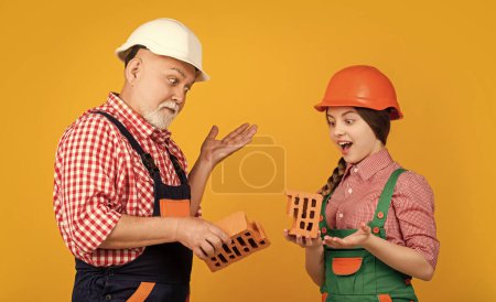 amazed child and granddad bricklayer in helmet on yellow background.