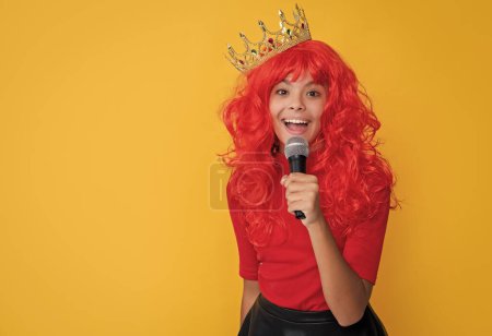 positive kid in crown with microphone on yellow background.