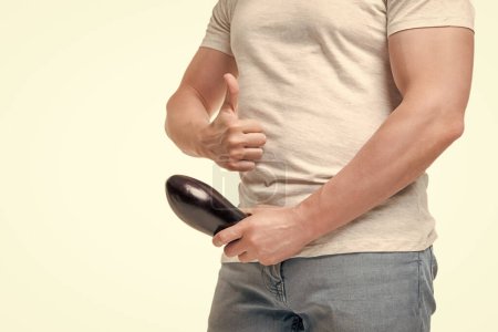 Man crop view giving thumb holding eggplant at crotch level imitating penis potency isolated on white.