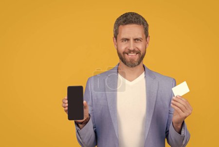 ecommerce concept. happy man paying online, ecommerce. man paying online hold phone and ecommerce card with copy space. man paying ecommerce online isolated on yellow. man paying online in studio.