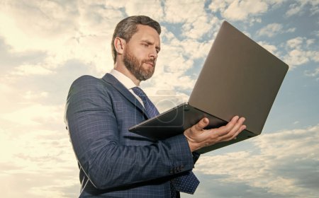 Professional man using laptop computer. Successful businessman working on computer. Serious computer user in suit. Sysadmin or system administrator sky background. Computer technology for business.