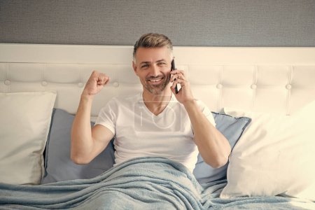 successful mature man in bed speaking on phone.