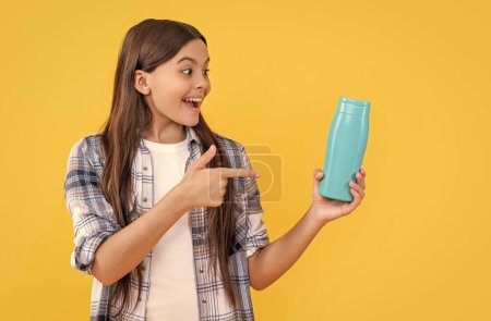 photo of amazed teen girl with shampoo cosmetics. teen girl with shampoo cosmetics isolated on yellow. teen girl with shampoo cosmetics in studio. teen girl with shampoo cosmetics on background.