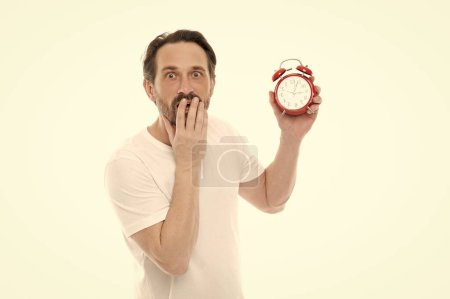 photo of worried man with alarm clock. man with alarm clock isolated on white. man with alarm clock in studio. man with alarm clock on background.