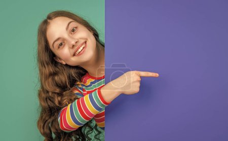 niño adolescente feliz detrás de papel azul en blanco con espacio de copia para publicidad. dedo índice.
