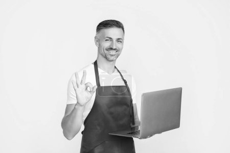 glad mature man in apron chatting on computer.